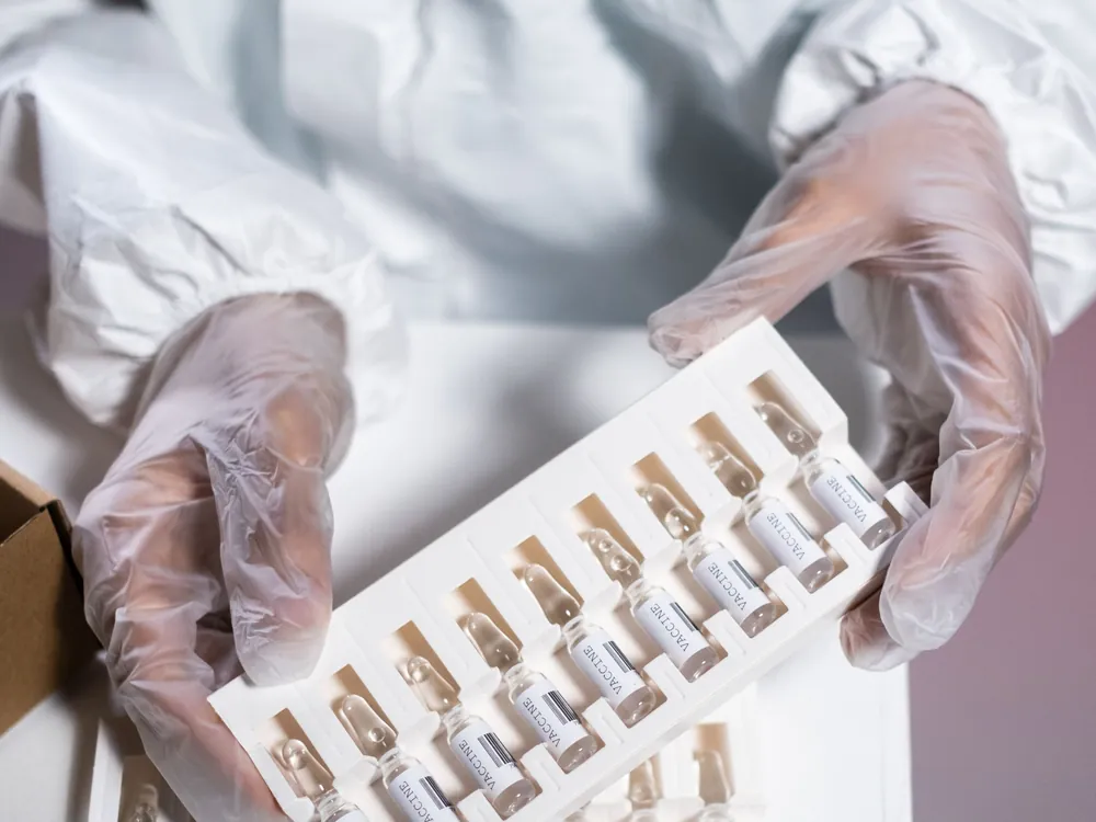 GMP operator in protective clothing handling pharmaceutical ampoules in a cleanroom environment